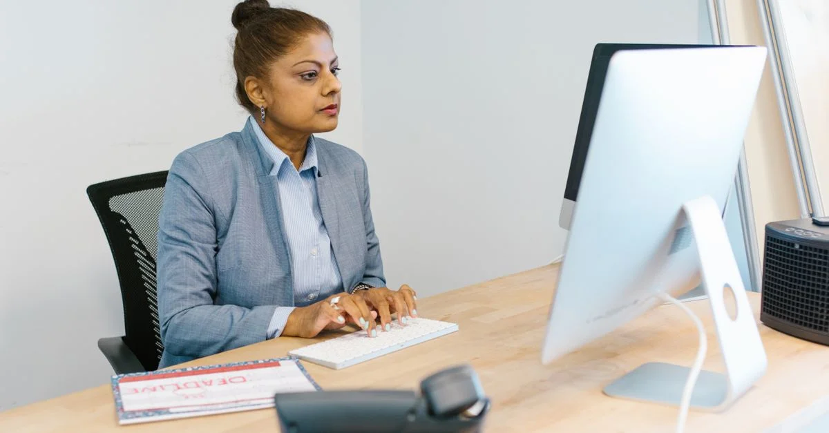 Femme concentrée travaillant avec assiduité à son bureau avec un ordinateur et des documents.