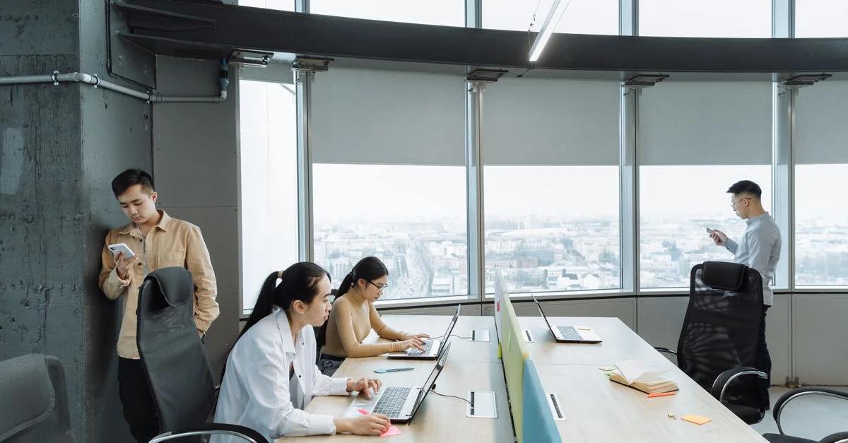 Scène de bureau contemporain avec des collègues asiatiques travaillant sur des ordinateurs portables et des smartphones.