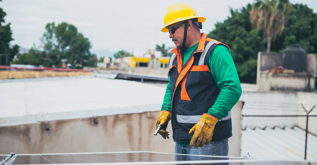 Un technicien solaire en tenue de protection inspectant des panneaux solaires sur le toit en plein air.