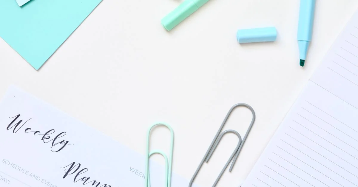 Fournitures de bureau turquoise et blanches soigneusement rangées, comprenant un agenda hebdomadaire, des trombones et des stylos.