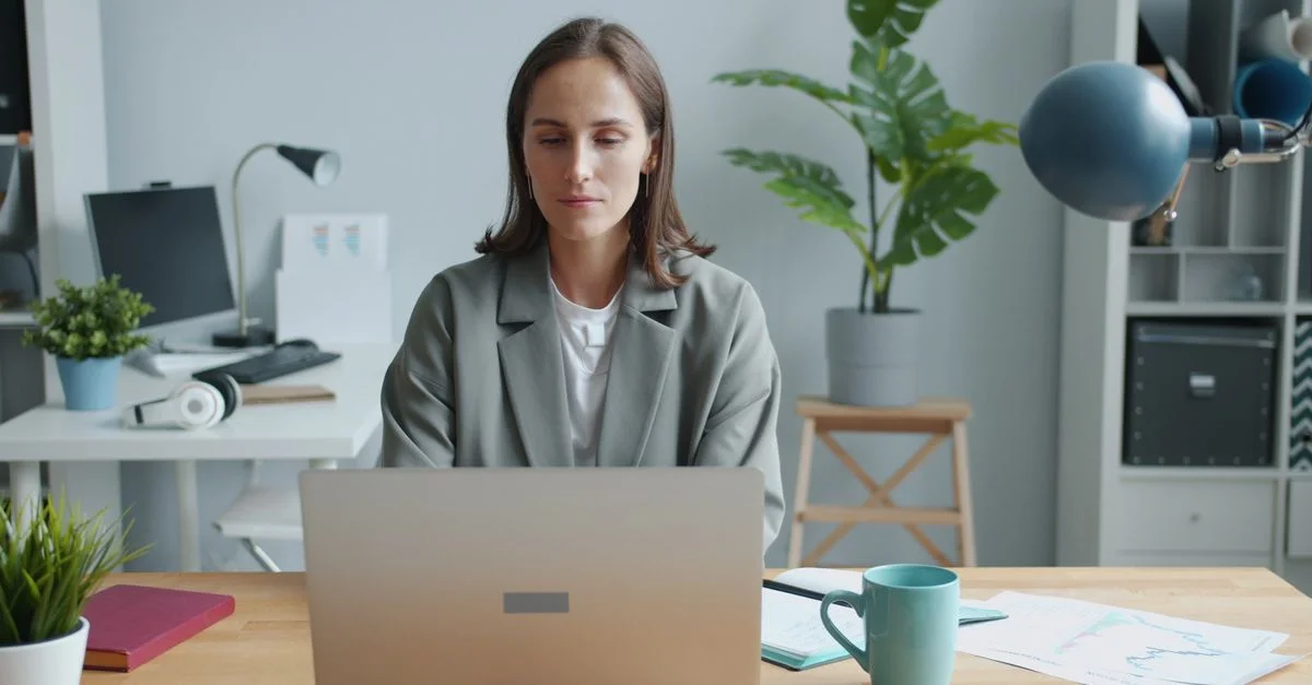 Femme travaillant à un bureau dans un environnement de bureau moderne, concentrée sur son ordinateur portable.