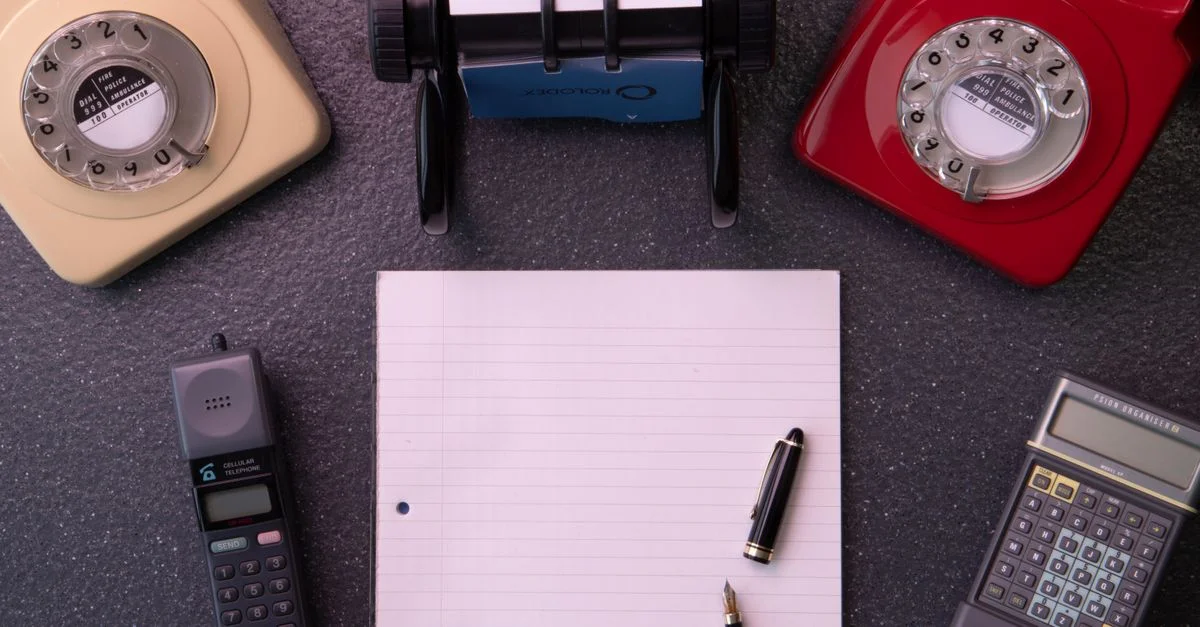 Équipement de bureau vintage avec téléphones à cadran, carnet de notes et composition à plat de calculatrice.