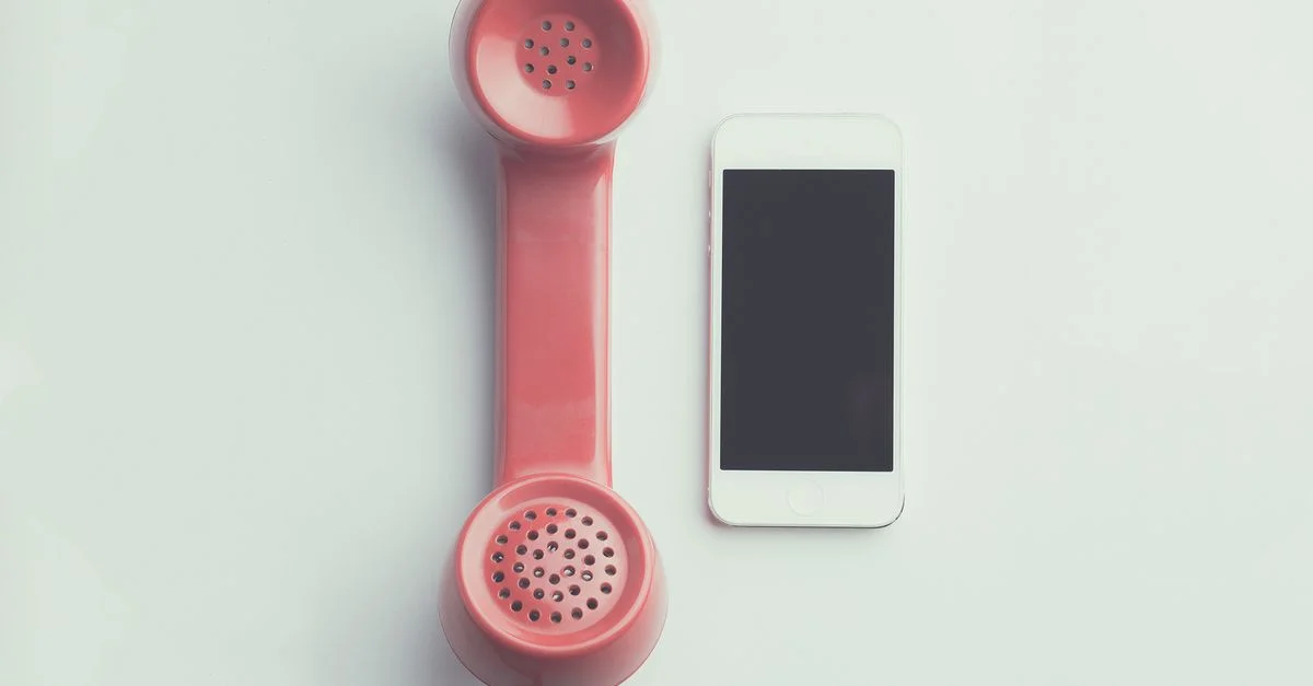 Comparaison d'un récepteur de téléphone vintage rose et d'un smartphone moderne sur un fond simple.