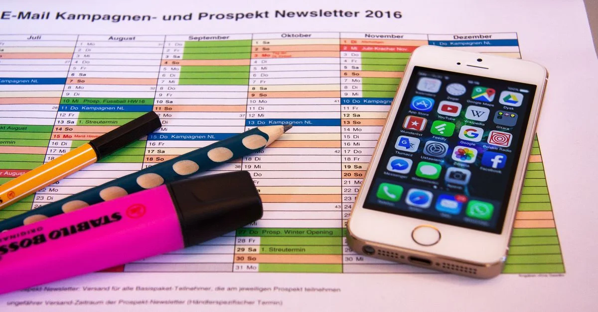 Un bureau avec un organiseur, des stylos et un smartphone affichant des icônes d'applications, idéal pour la productivité.