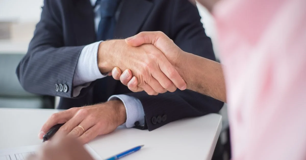 Deux hommes d'affaires se serrant la main autour d'une table, symbolisant un accord et un partenariat dans un environnement de bureau.