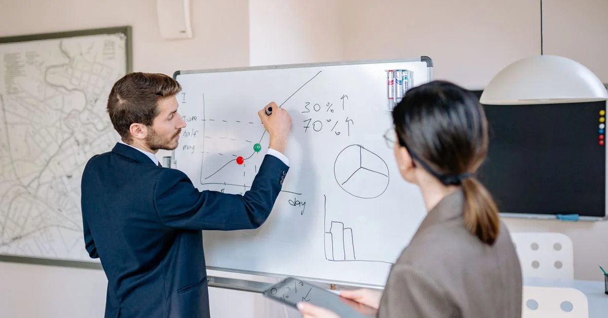 Deux professionnels d'affaires planifiant et discutant de la stratégie devant un tableau blanc dans un bureau moderne.