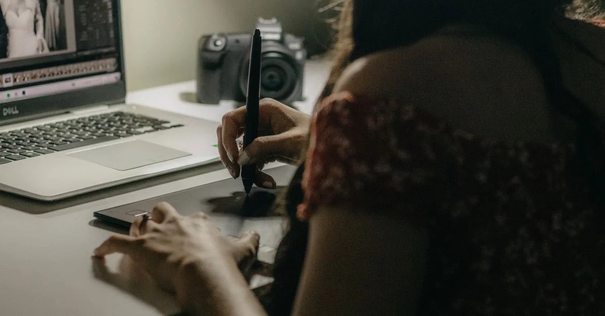 Une femme utilise une tablette graphique et un ordinateur portable pour retoucher des photos dans un espace de travail moderne.