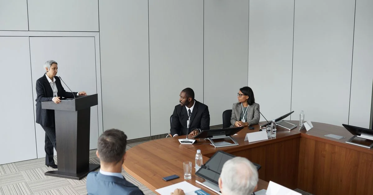 Groupe divers de professionnels dans un cadre de réunion formel avec un intervenant au podium.