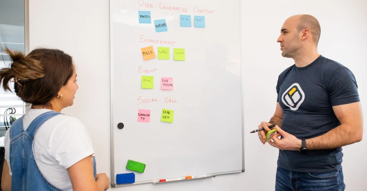 Des collègues échangent des idées sur la stratégie de projet en utilisant des notes sur un tableau blanc au bureau.