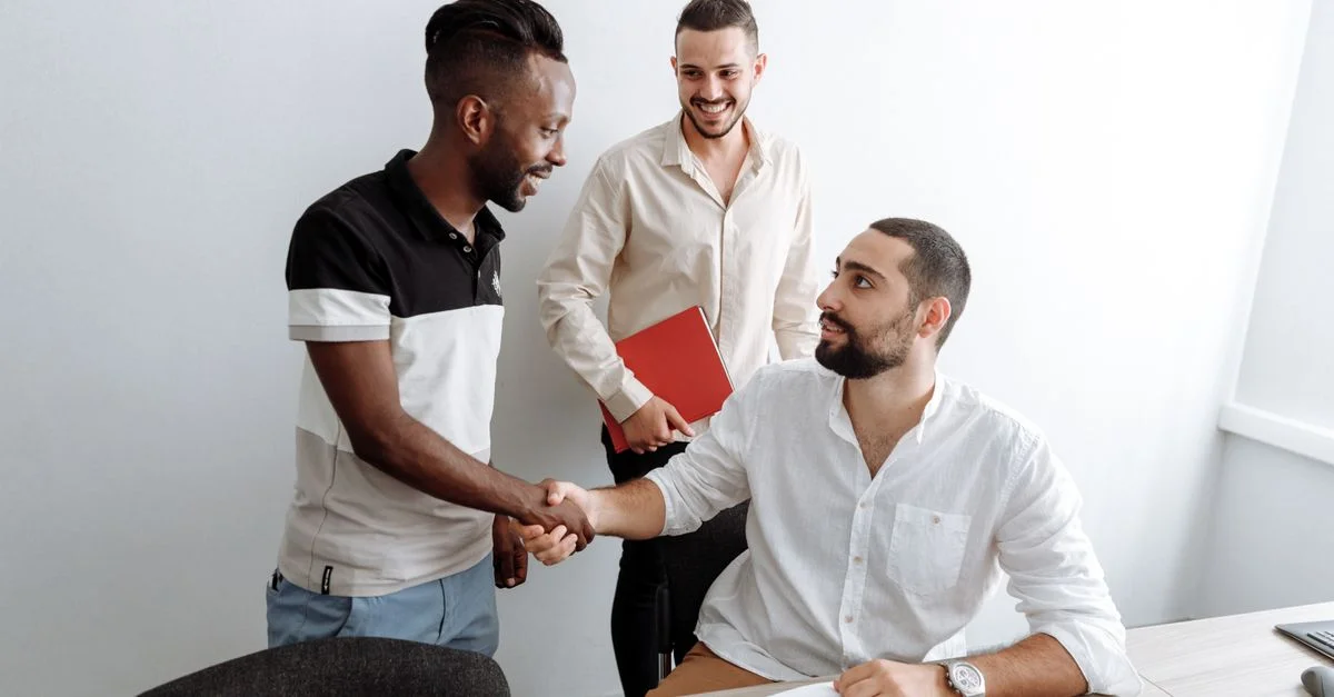 Trois hommes dans un bureau engagés dans une poignée de main amicale, illustrant le travail d'équipe et la collaboration.