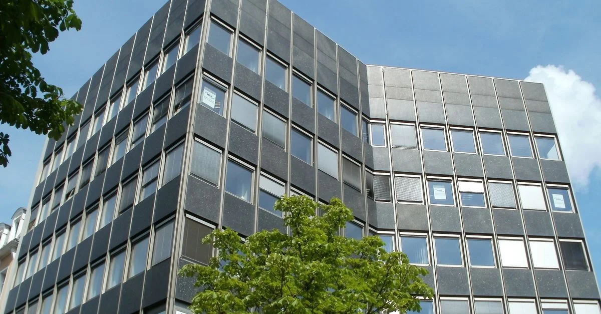 Vue en contreplongée d'un bâtiment de bureau moderne sous un ciel bleu clair, encadré par des arbres verts.
