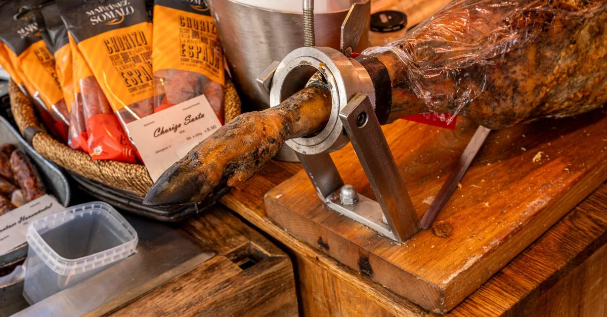 Gros plan sur des charcuteries, y compris du jambon espagnol et du chorizo, en vitrine d'une épicerie fine.