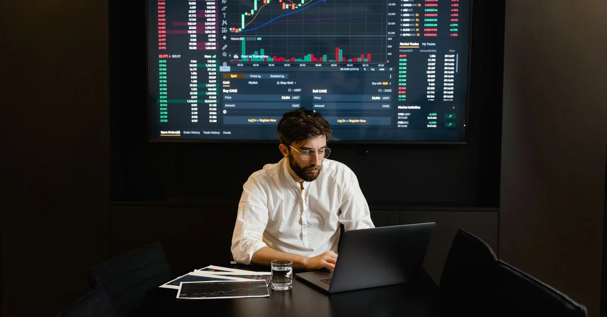 Homme d'affaires concentré analysant les données du marché boursier sur un ordinateur portable avec des graphiques financiers affichés à l'écran.
